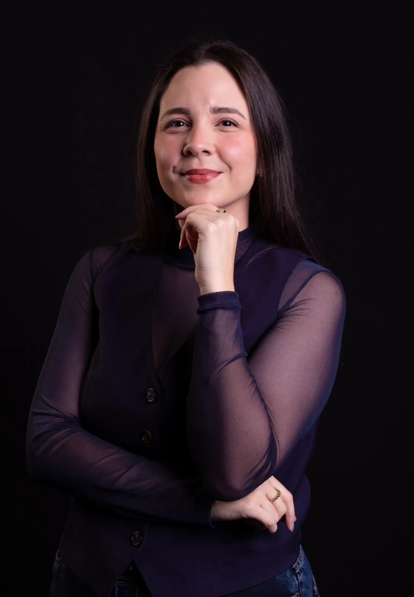 Dra. Vitória Rollim sorrindo, com a mão no queixo, sobre fundo escuro
